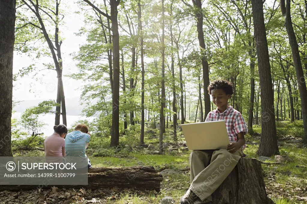 Boy using a laptop in a forest