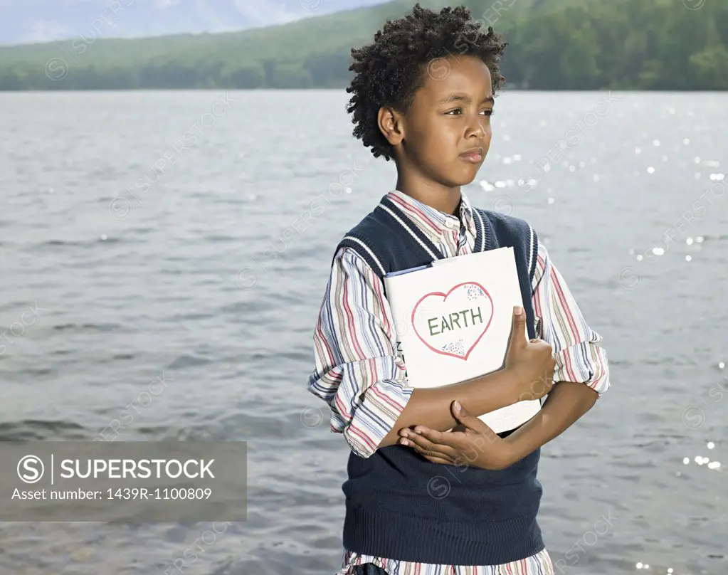 A boy holding a book by a lake