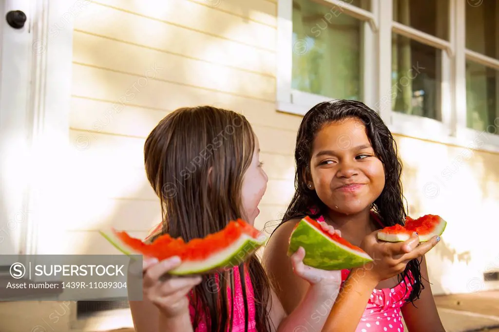 Two smiling girls sitting on house porch with slices of watermelon