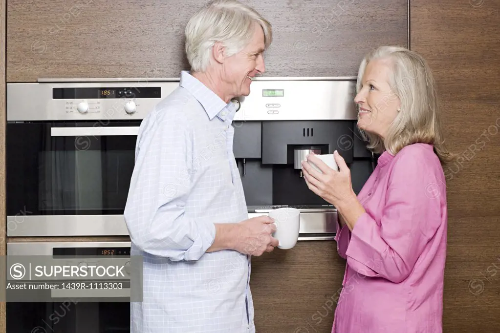 Middle aged couple standing in kitchen with cups of coffee