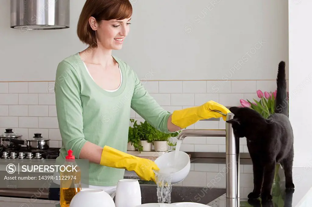 Woman washing up with cat by sink
