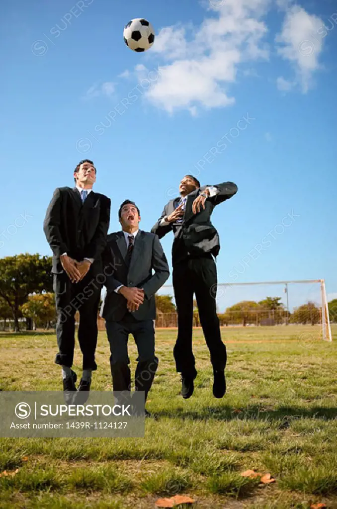 Businessmen jumping for football