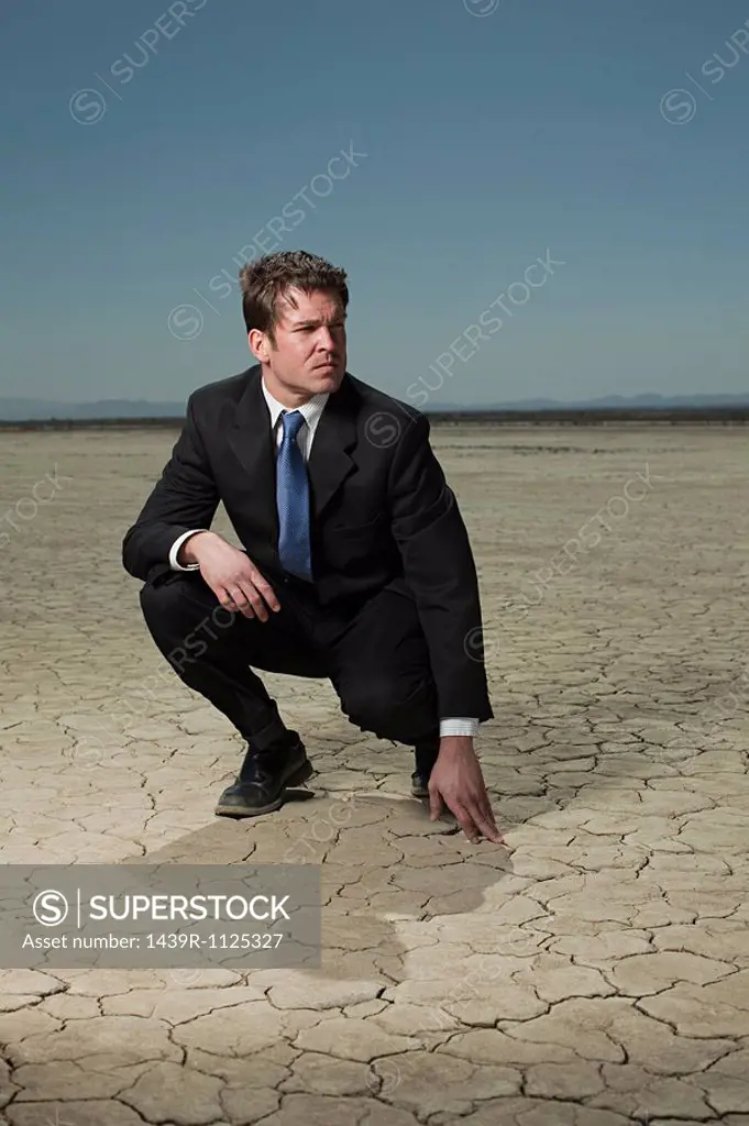 Businessman crouching in desert landscape