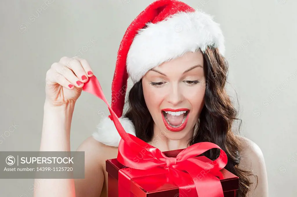 Young brunette woman wearing Santa hat opening Christmas present