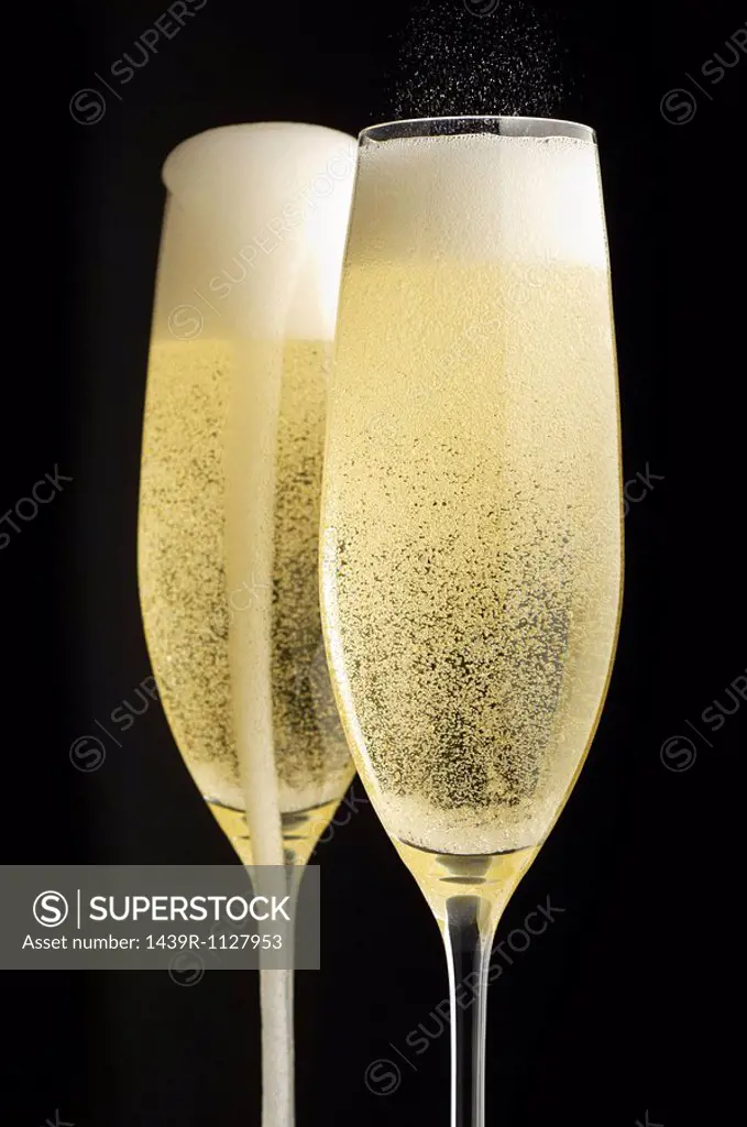 Two full champagne glasses with champagne overflowing