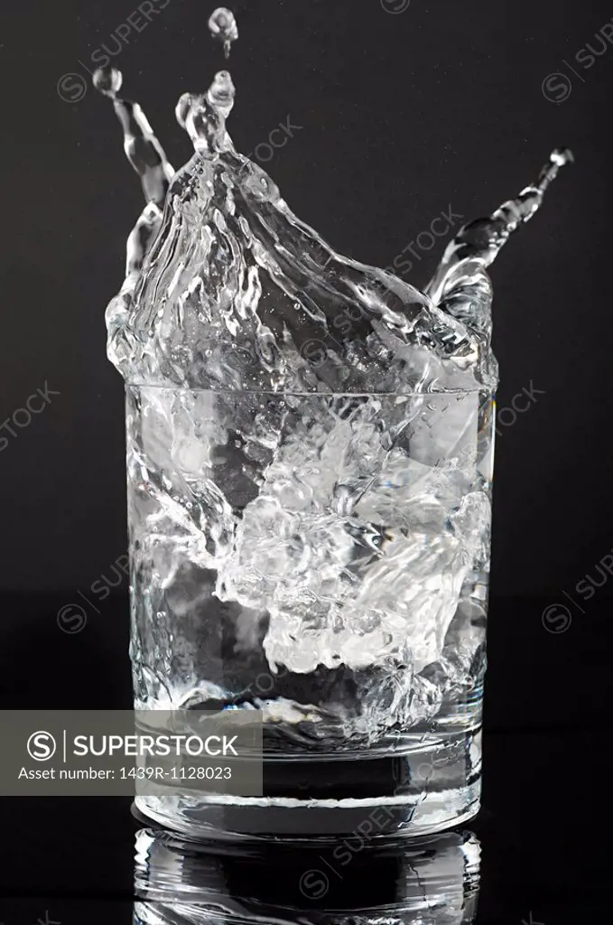 Ice cube splashing in a tumbler of gin and tonic