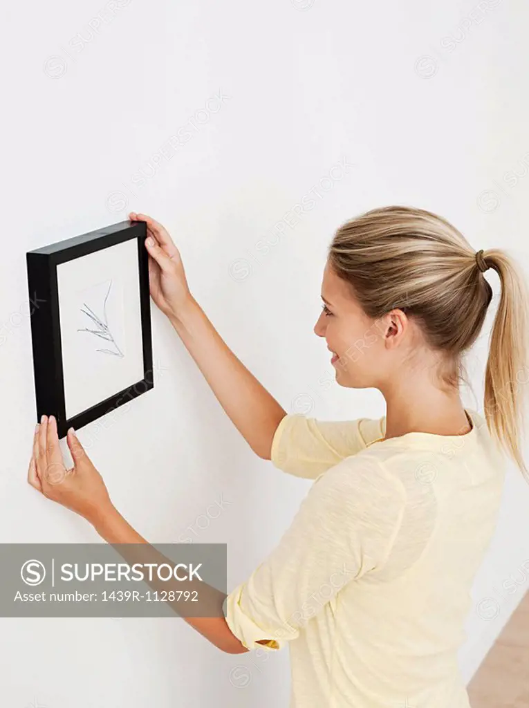 Young woman hanging picture on wall
