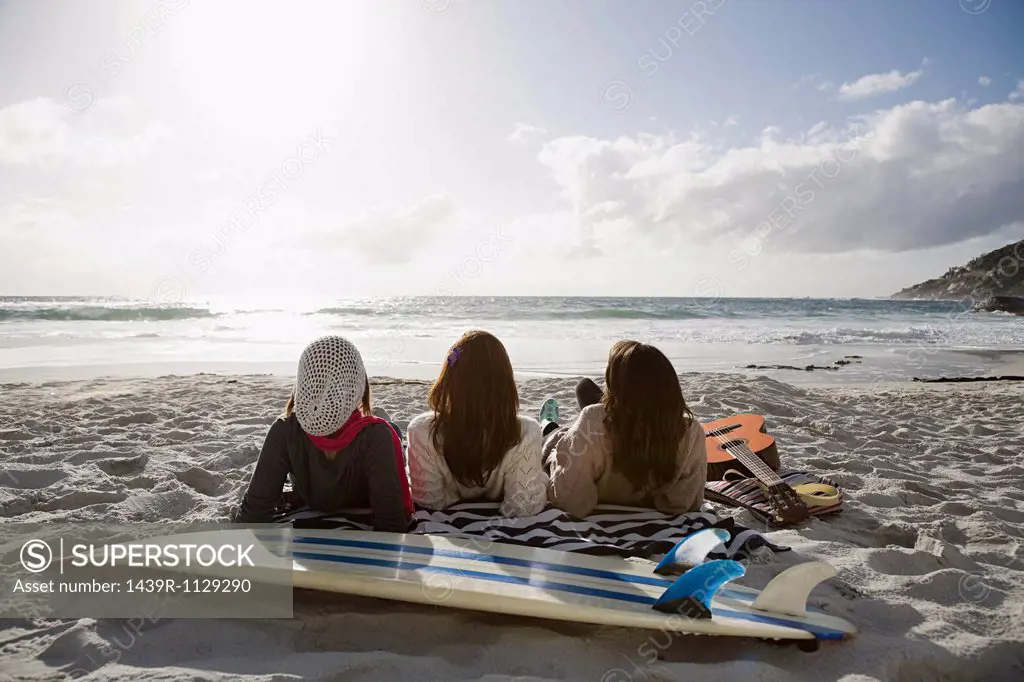 Three girls lying on beach with surfboard