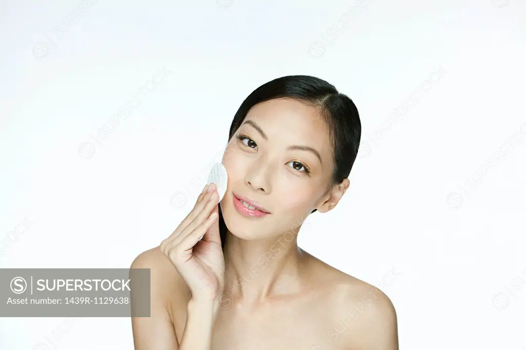 Young woman using cotton pad on face
