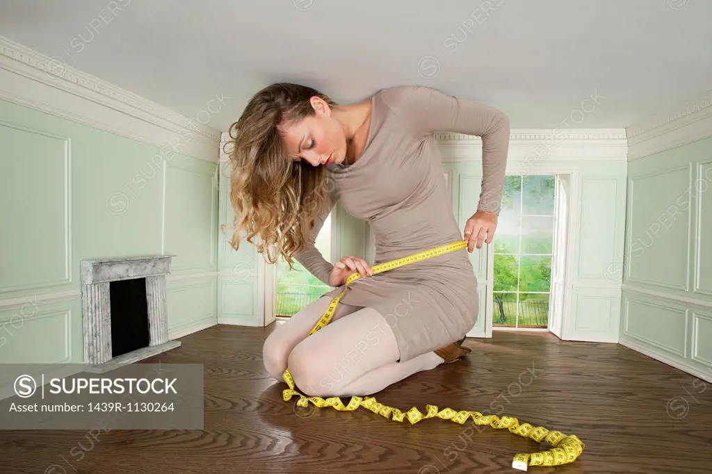 Young woman in small room measuring her waist