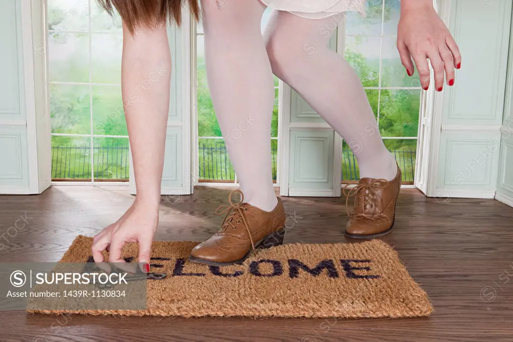 Woman picking up key on welcome mat in small room