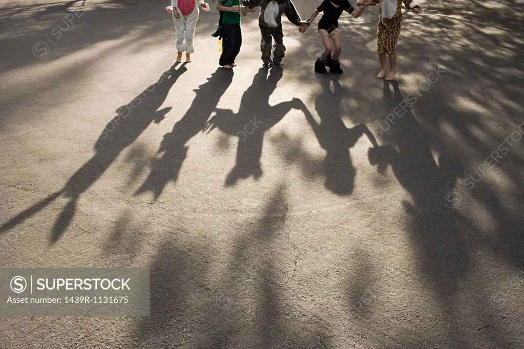 Five children in fancy dress holding hands, casting shadow