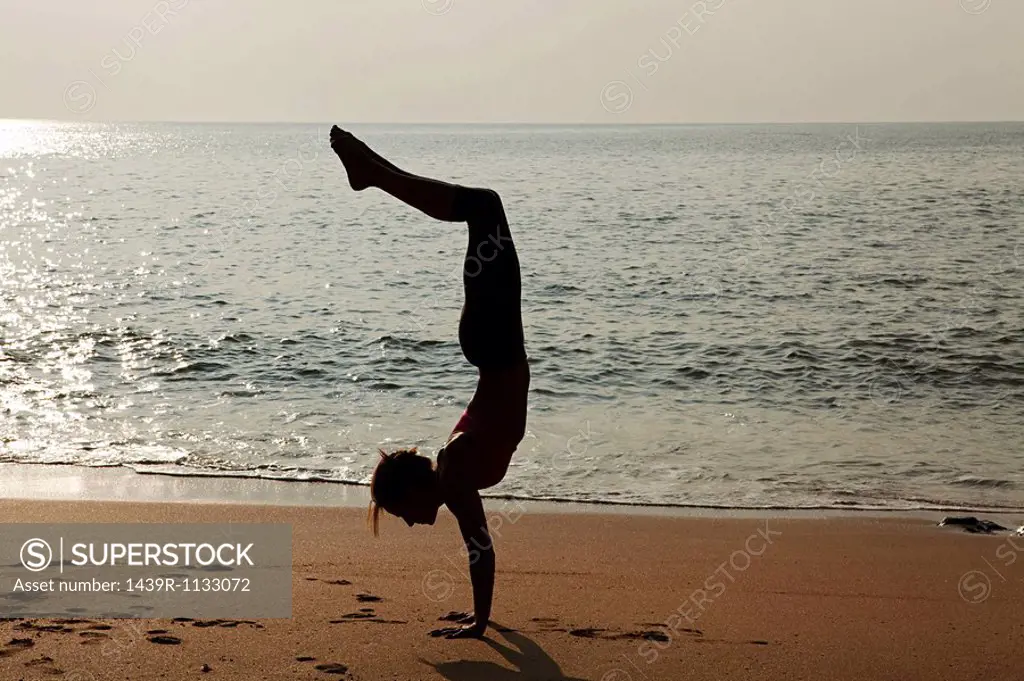 Woman practicing yoga on a beach at sunset