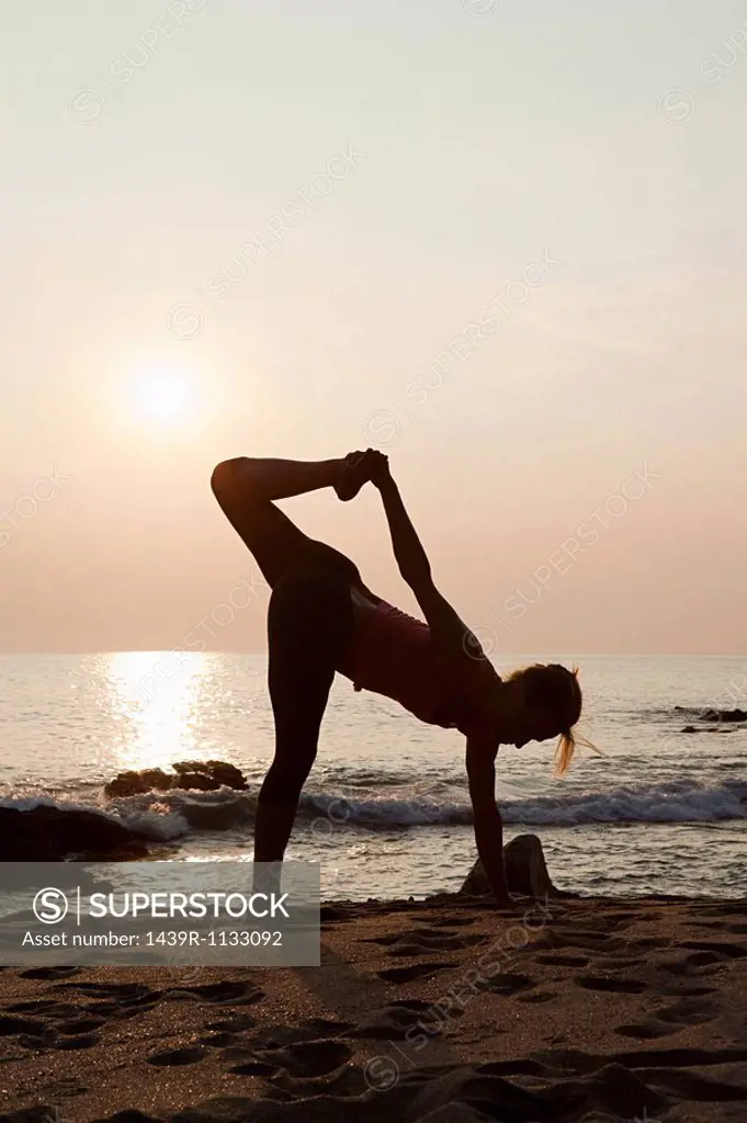 Woman practicing yoga on a beach at sunset