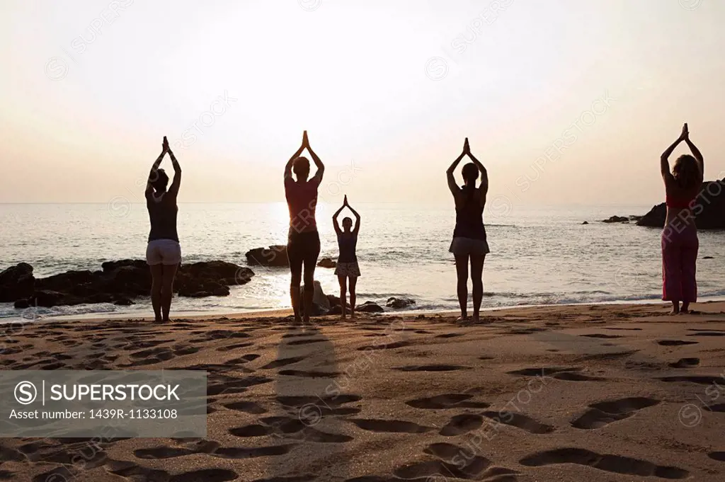 Women practicing yoga on beach at sunset