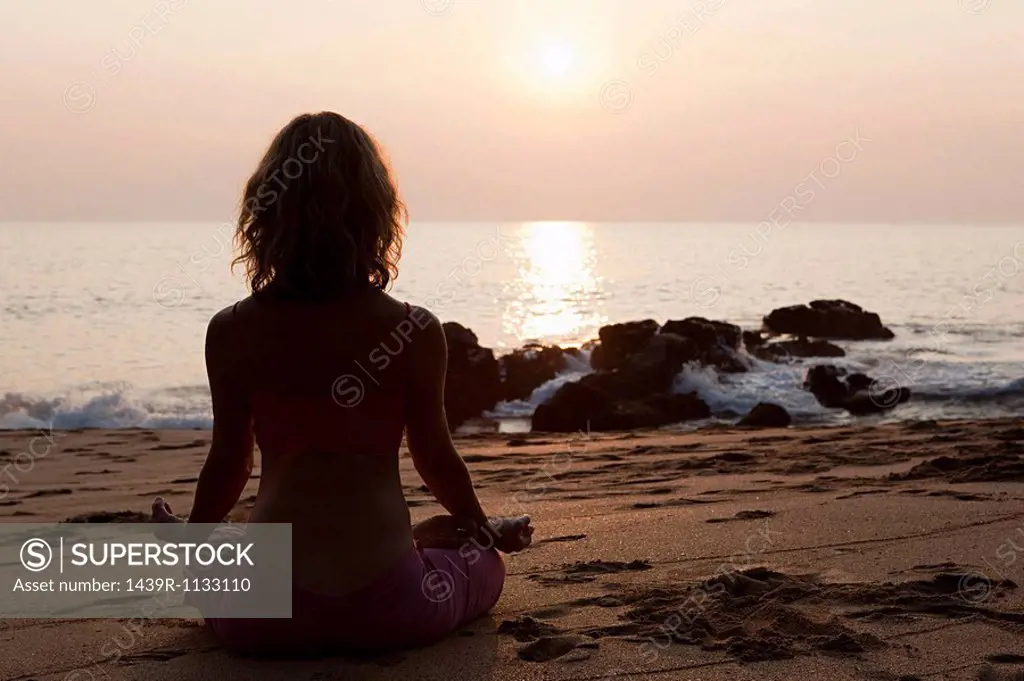 Woman practicing yoga on beach at sunset