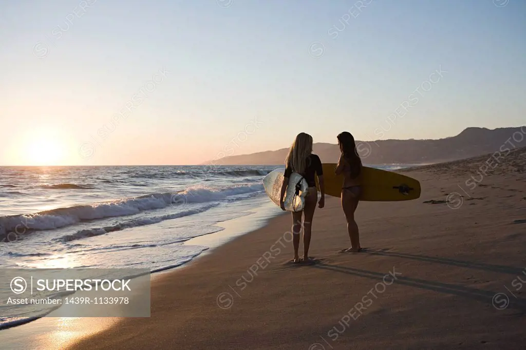 Female surfers by the sea at sunset