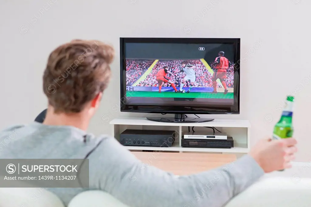 Young man watching football on television with beer bottle