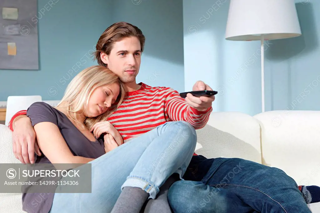 Young couple watching television, woman sleeping
