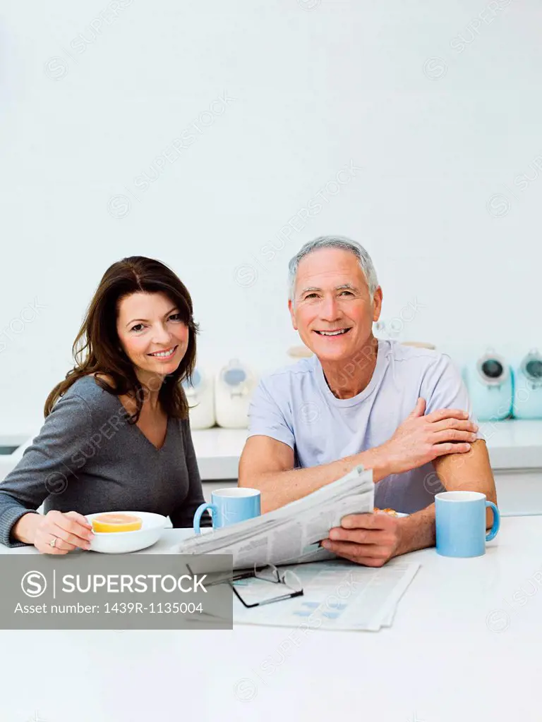 Mature couple having breakfast, reading newspaper