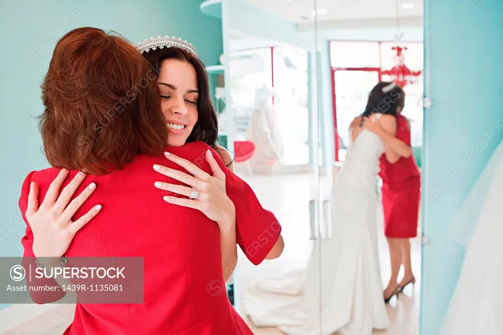 Daughter trying on wedding dress, embracing mother