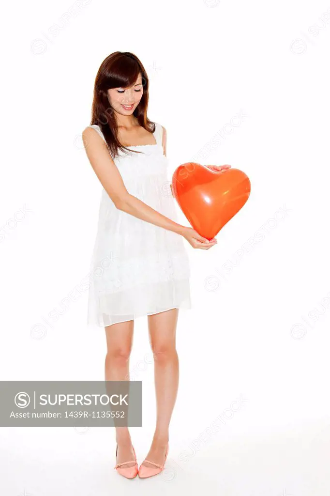 Woman holding red heart shaped balloon, studio shot