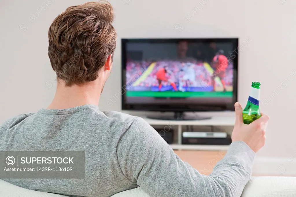 Young man watching football on television with beer bottle