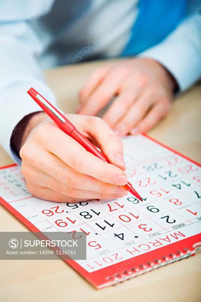 Office worker marking calendar with red pen