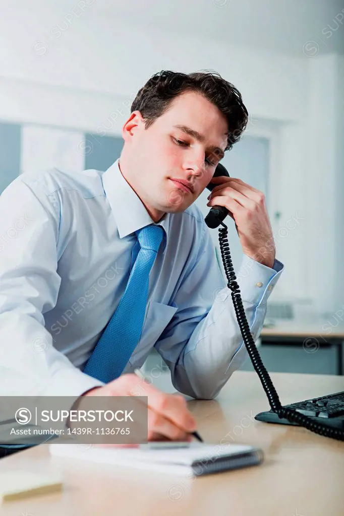 Office worker on telephone call, writing in notebook