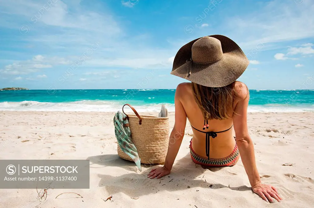 Woman sitting on sandy beach, Mustique, Grenadine Islands