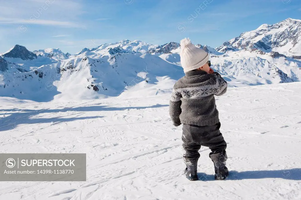 Young boy standing looking at mountains in snow