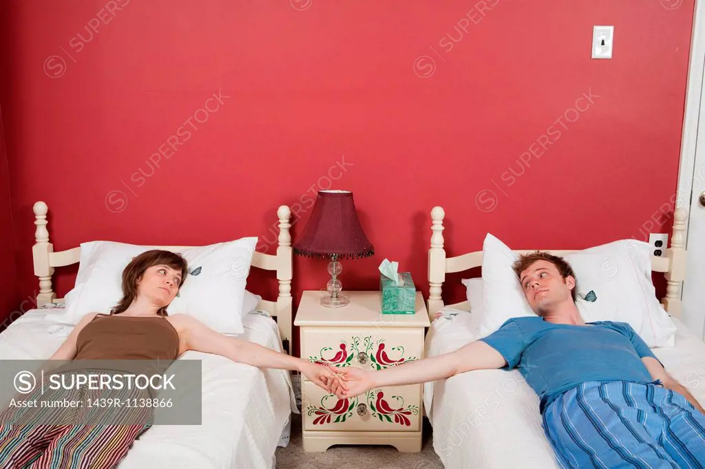 Young couple lying on single beds, holding hands