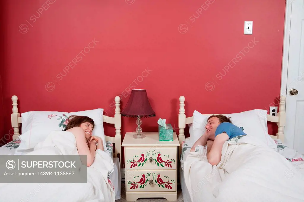 Young couple smiling at each other in single beds