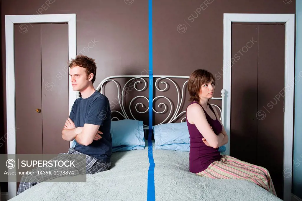 Young couple sitting on bed separated by blue line