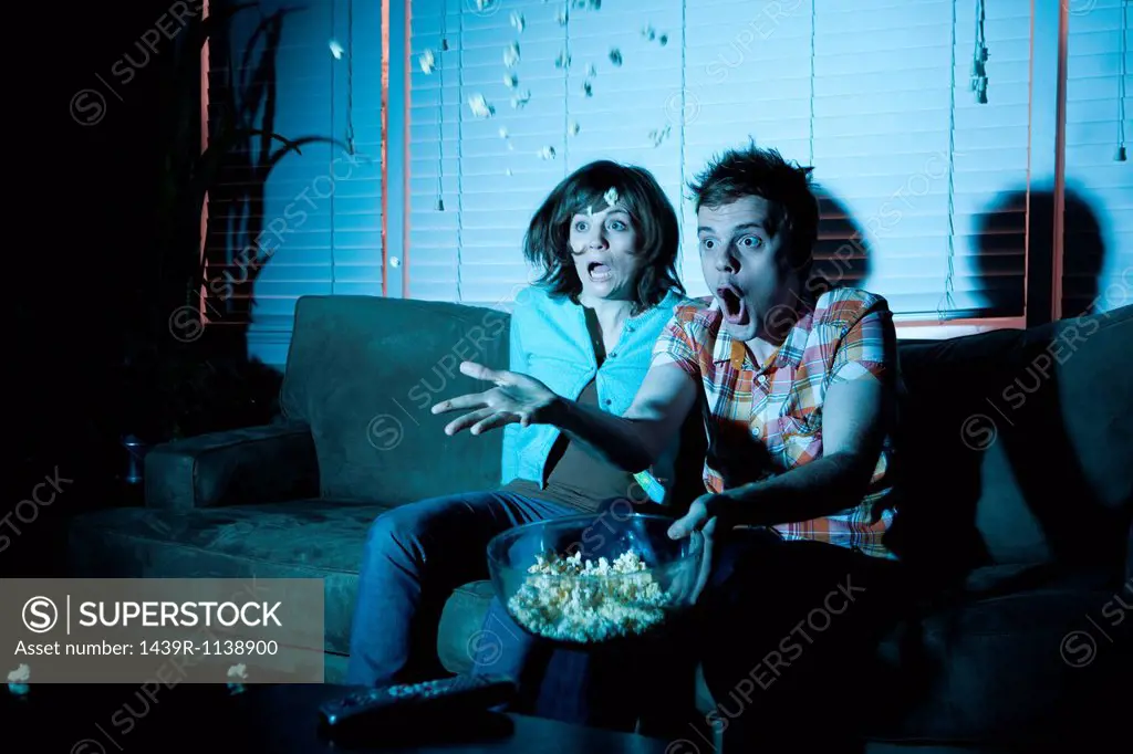 Young couple watching tv, man throwing popcorn