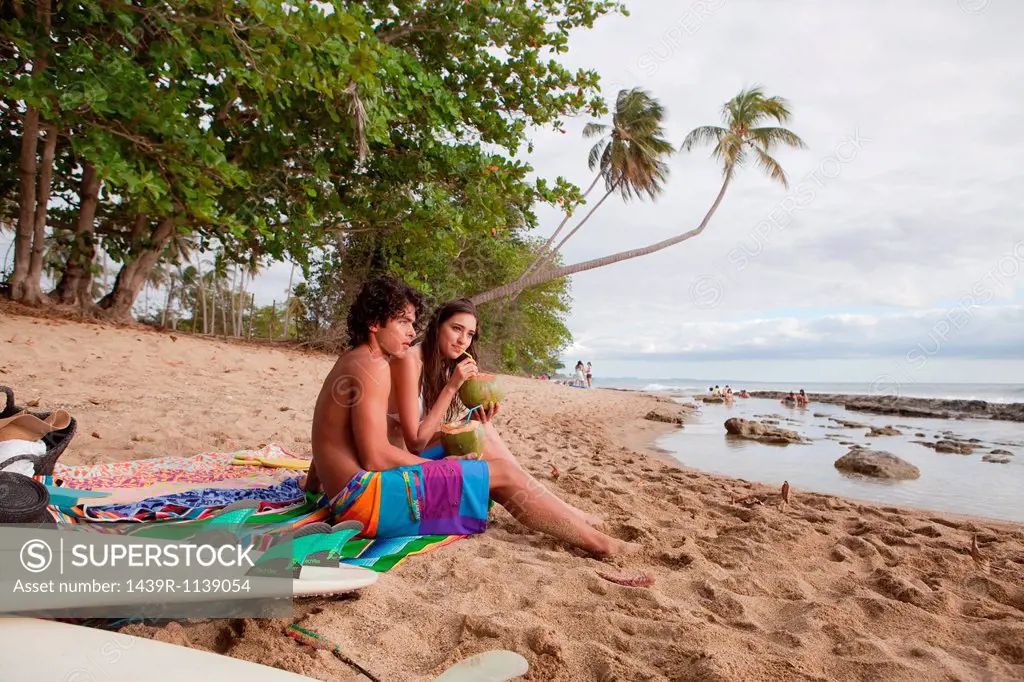 Young couple sitting on beach drinking coconut milk