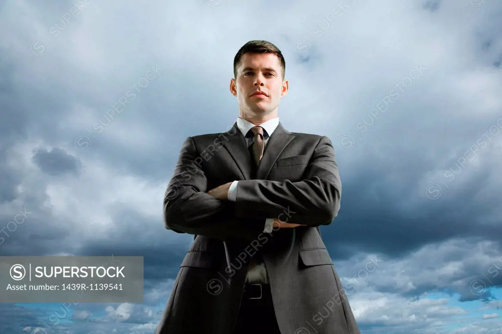 Businessman against storm cloud with crossed arms, low angle