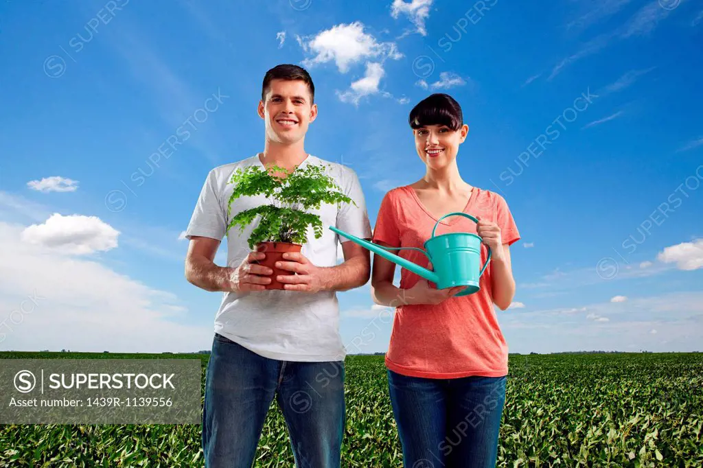 Couple in field holding plant and watering can