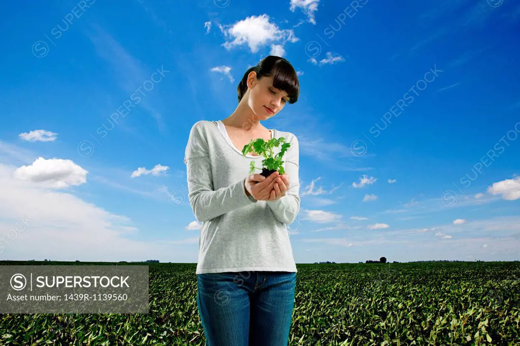 Young woman holding plant in field