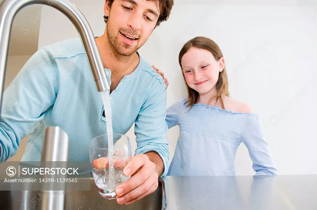 Young man filling glass of water for daughter