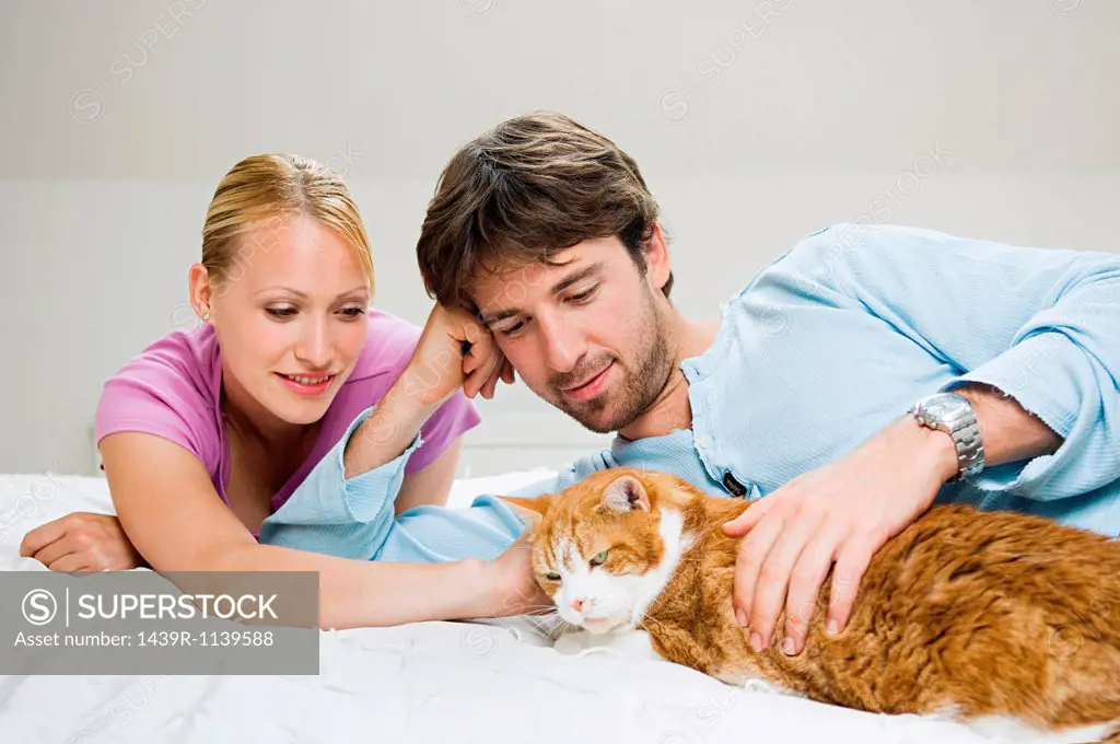 Young couple stroking cat on bed