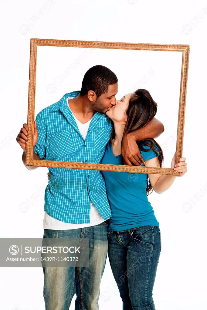 Mixed race couple kissing inside picture frame against white background