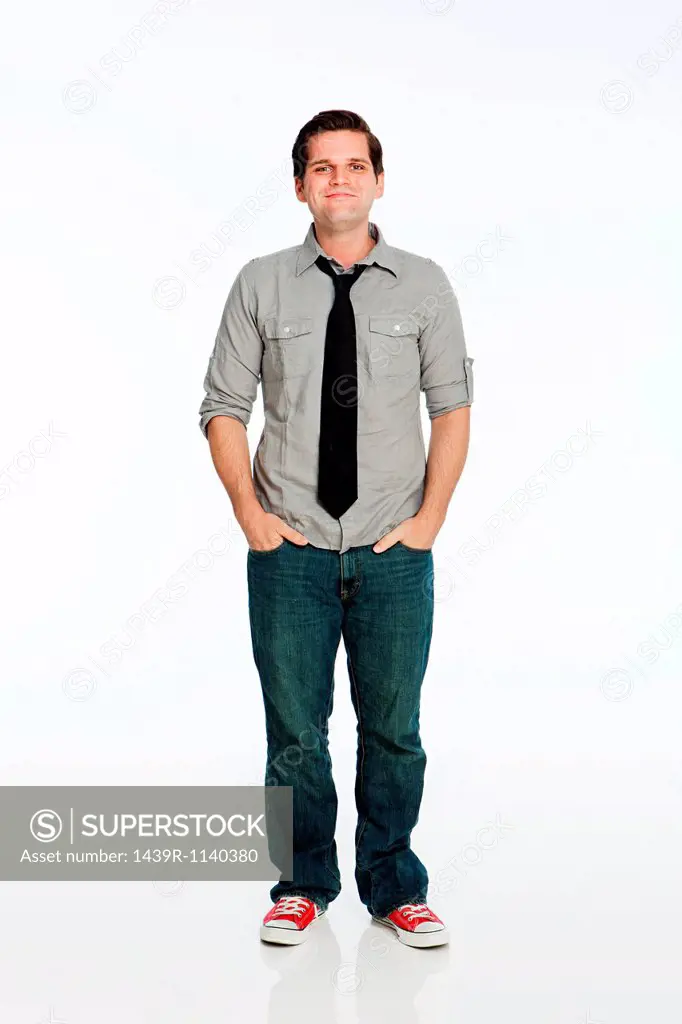 Young man with hands in pockets against white background