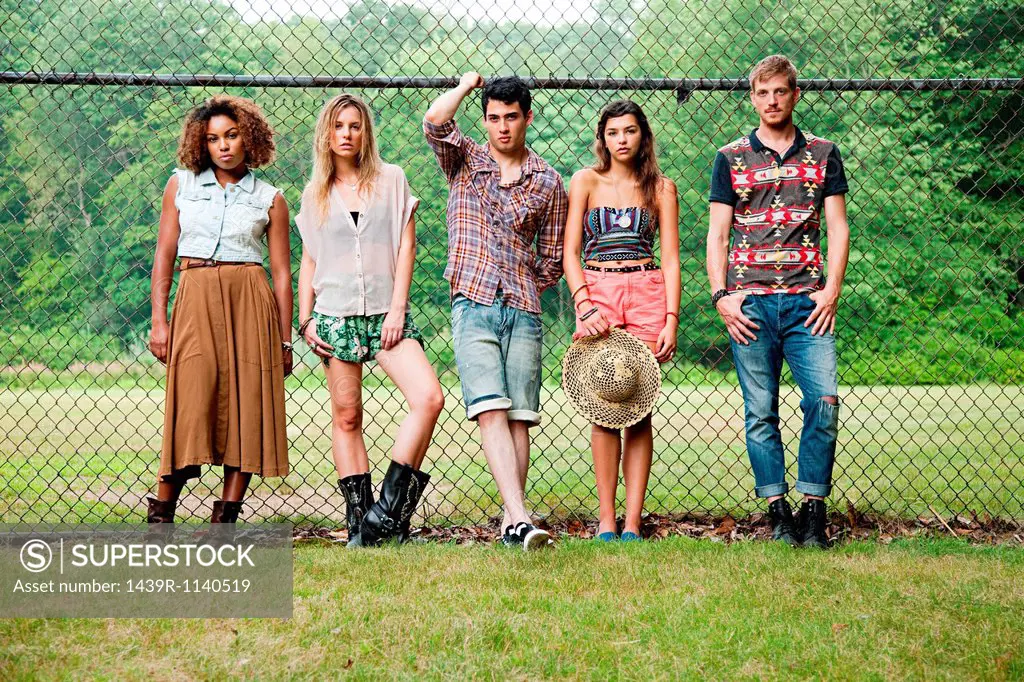 Portrait of friends standing against chain link fence