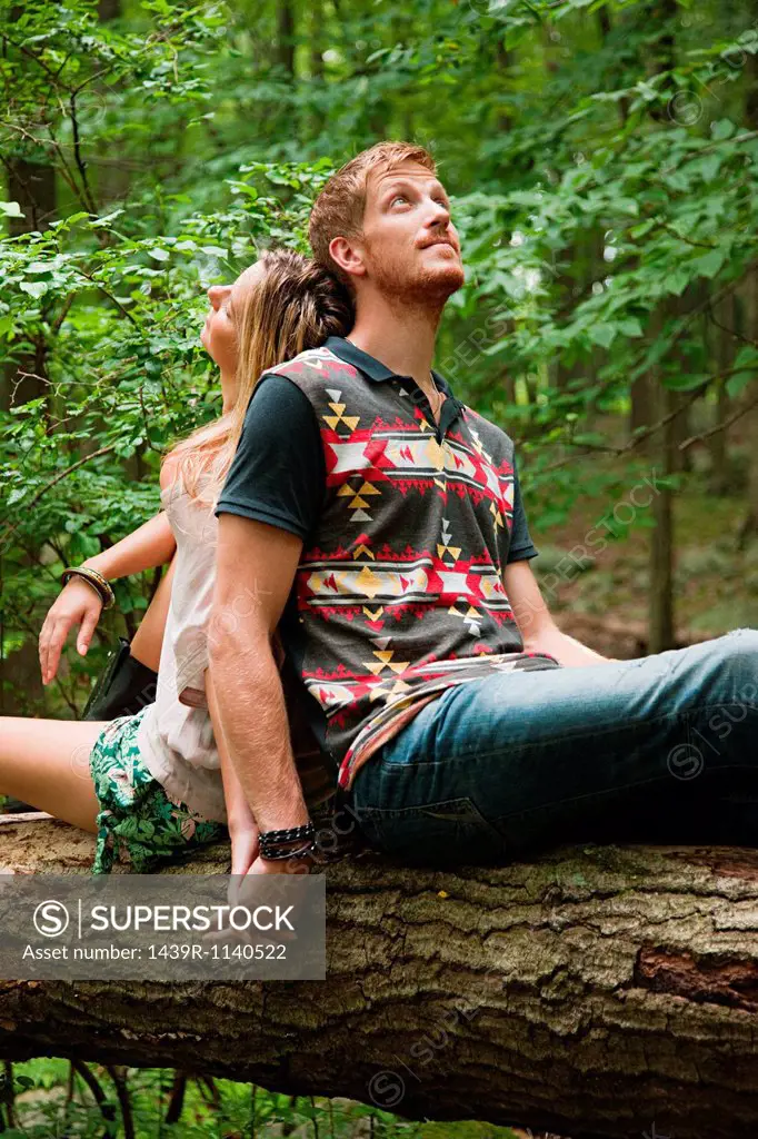 Couple leaning against each other on log in forest