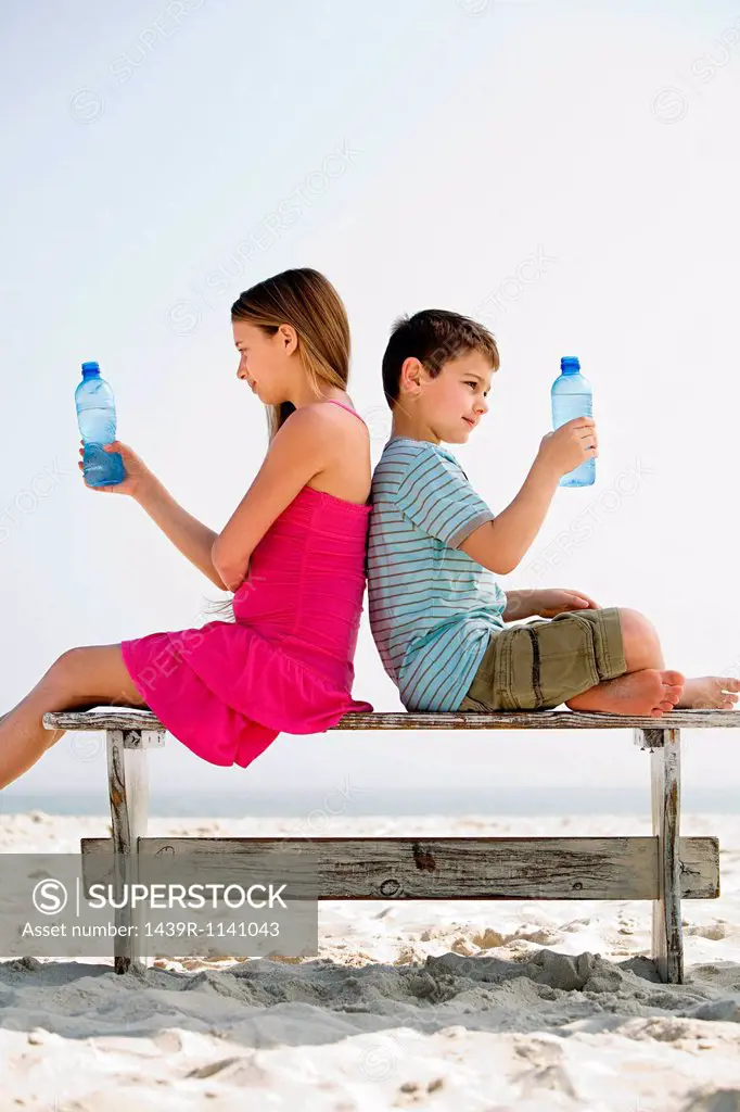 Girl and boy holding bottles of water on a beach