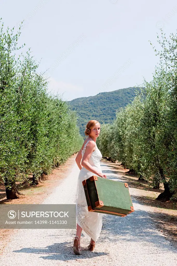Bride carrying suitcase on country road