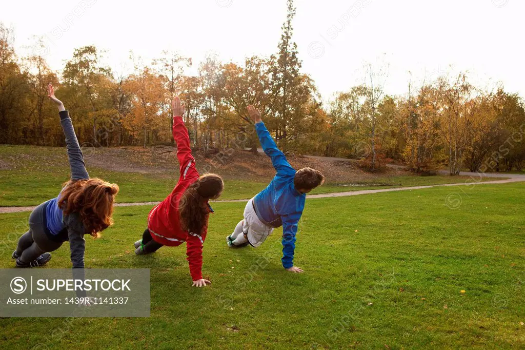 Three young friends stretching on grass in park