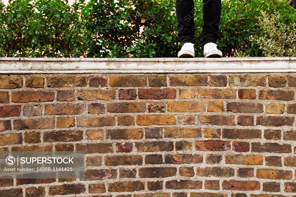 Woman in jeans standing on top of wall, low section