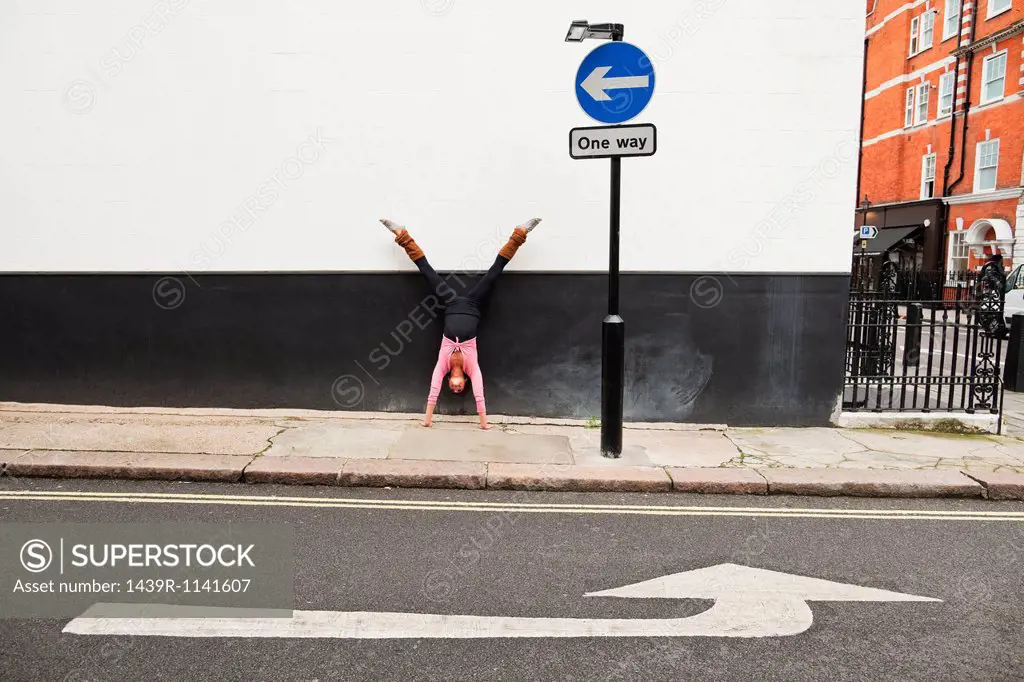 Woman performing handstand on pavement